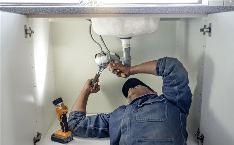 Plumber repairing pipes beneath a bathroom sink in Santa Clara